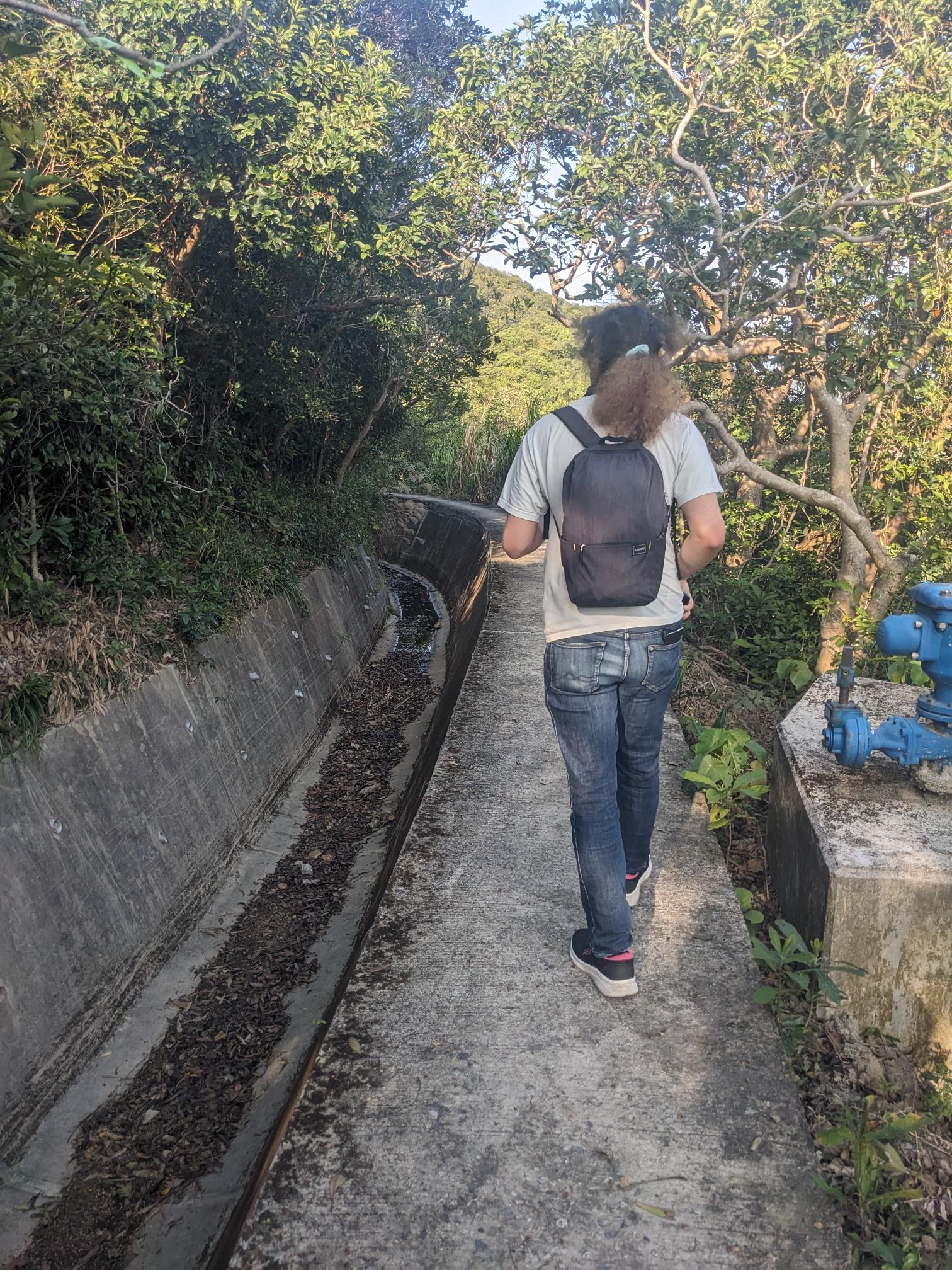 A white person with long fluffy hair walks on the edge of a canal. A white person with long fluffy hair walks on the edge of a canal.