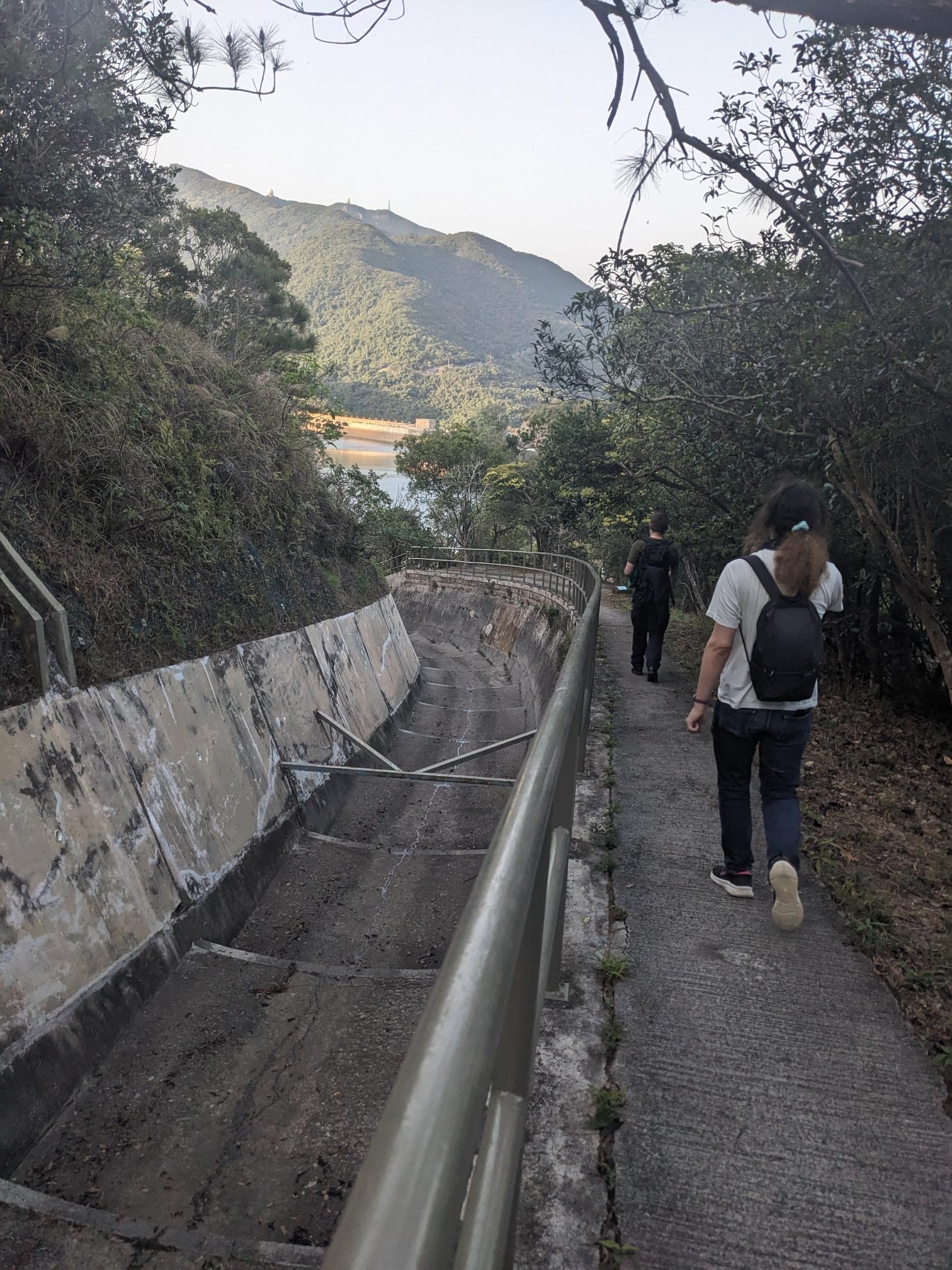 Two people walk along a canal. A lake ik the background. Two people walk along a canal. A lake ik the background.