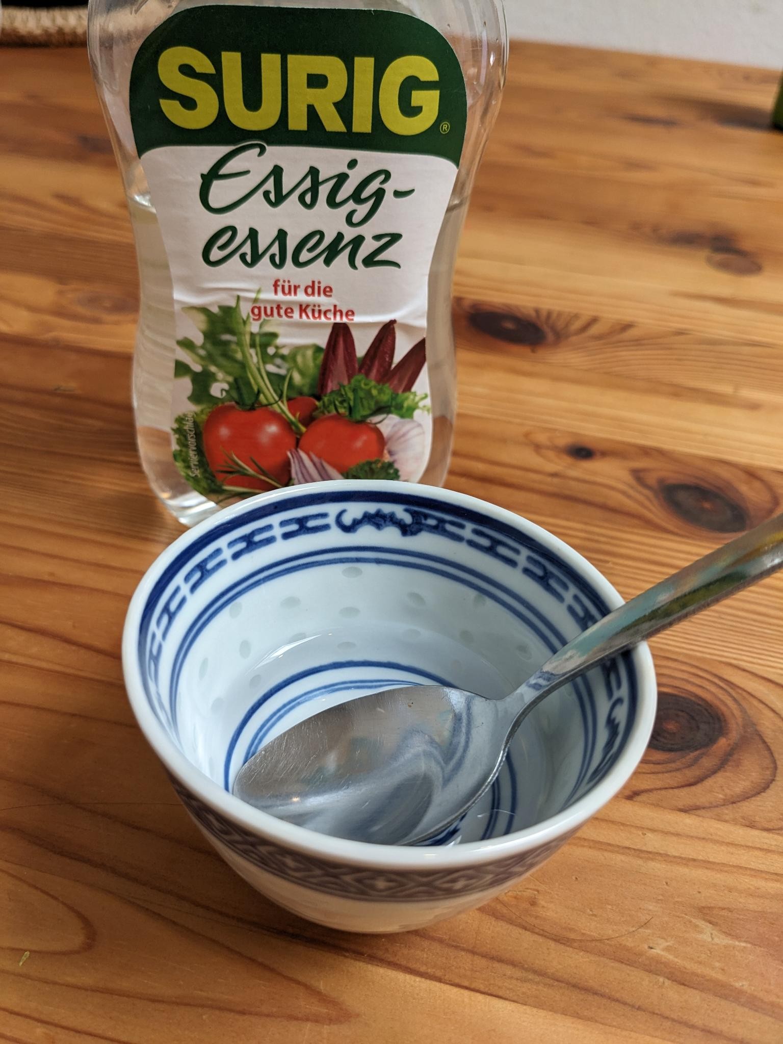 A small bowl that contains a clear liquid. Behind that is a bottle of distilled vinegar.