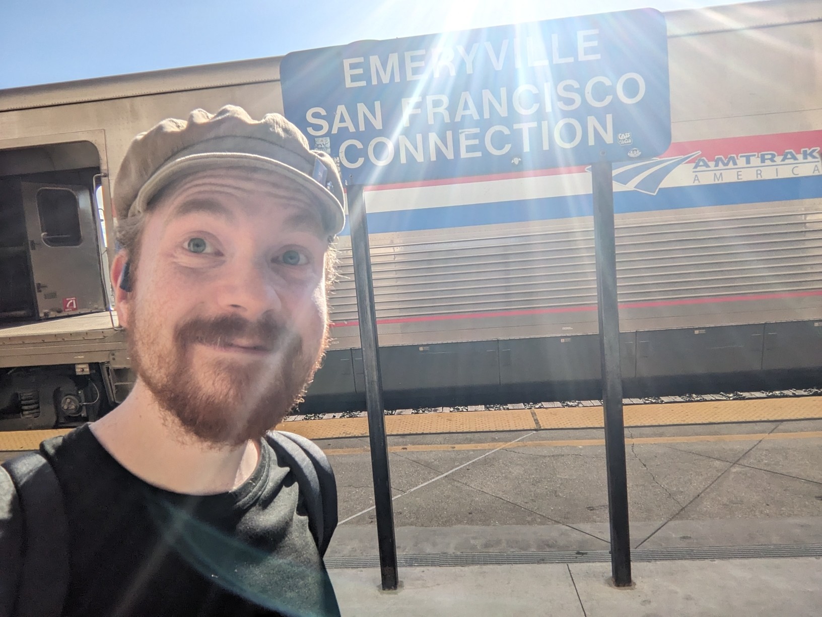 I'm smiling, at a sign labelled "Emeryville, San Francisco Connection".