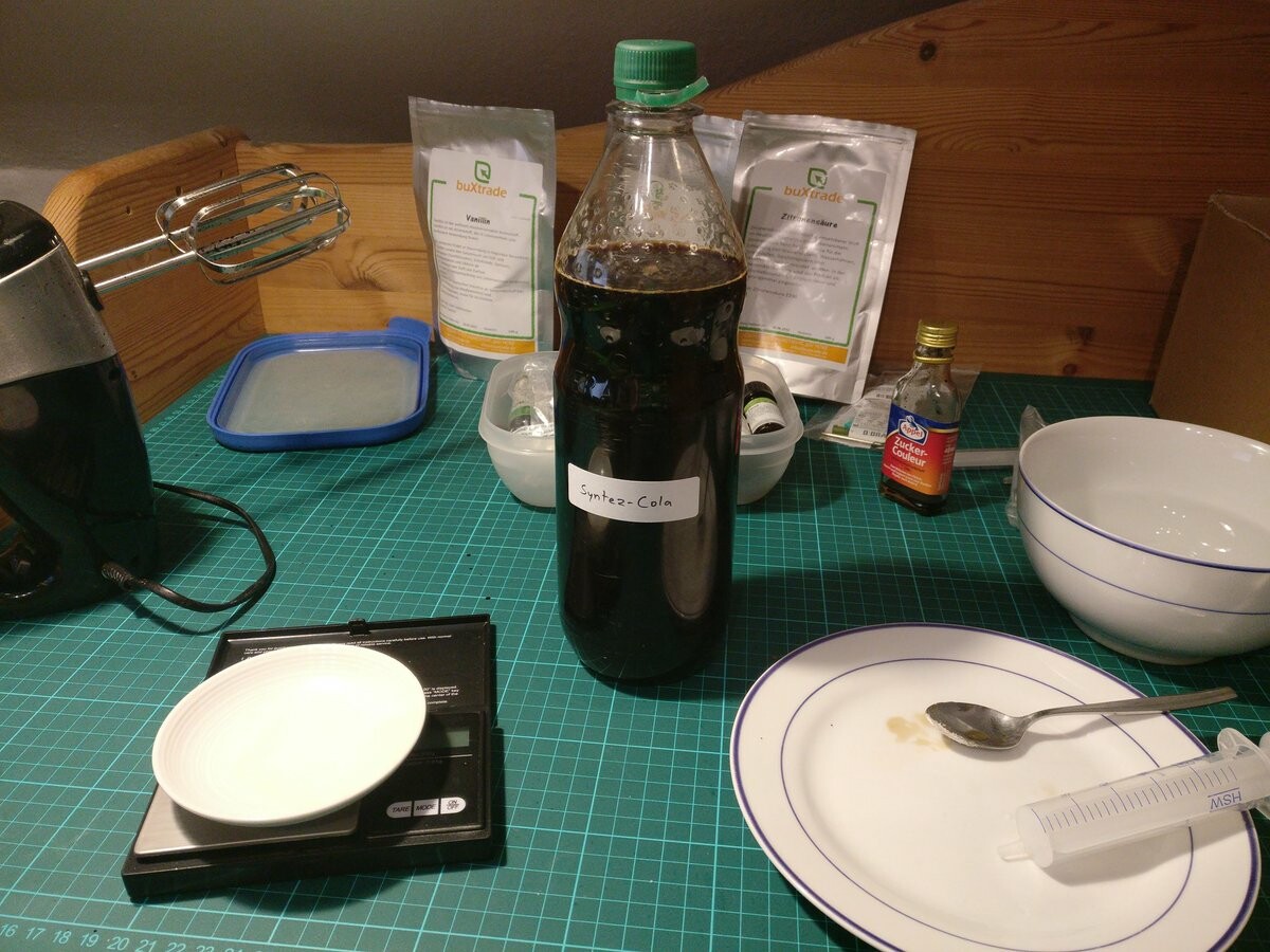 A bottle of cola sirup in the middle of equipment and ingredients that were used to make it.