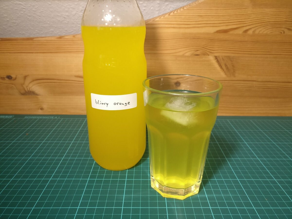A yellow soft drink in a bottle and in a glass.
